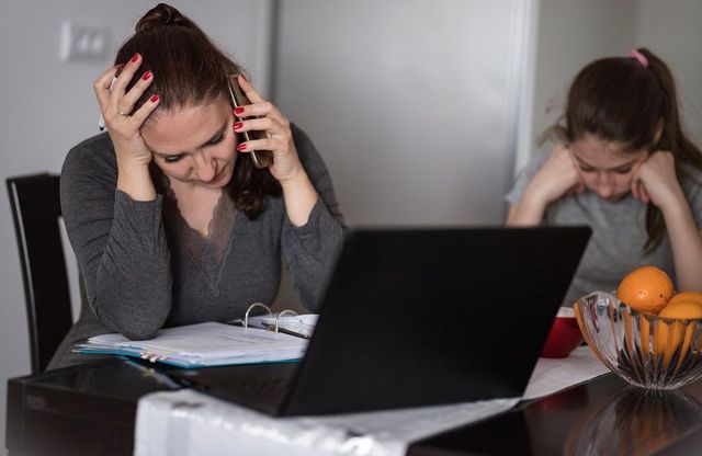 Photo d'une mère qui se tient la tête car sa fille subit du harcèlement à l'école. Elle est en train de téléphoner. Sa fille est à côté et se tient la tête ce qui manifeste sa souffrance. Image qui représente l'aide qu'un psychologue en ligne peut apporter aux parents lorsque leur enfant se fait harceler à l'école