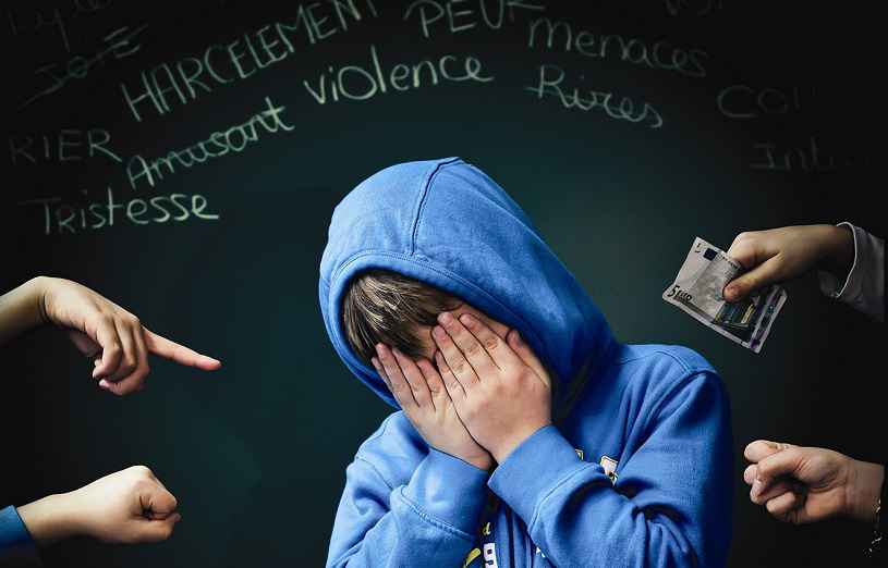Photo d'un garçon qui se tient la tête dans les mains car il subit du harcèlement à l'école. Il est écrit sur un tableau derrière lui : harcèlement, menaces, violence, tristesse. Il y a des poings et un doigt pointé vers lui représentant la violence physique et psychologique qu'il subit. Il y aussi de l'argent qui signifie qu'il est victime de racket à l'école